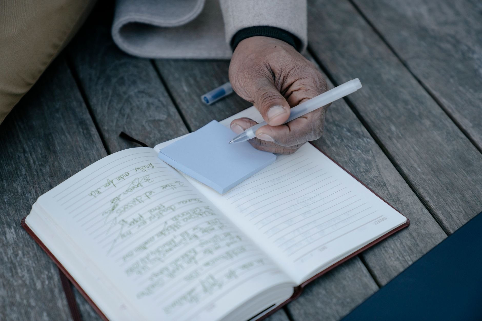 Person writing notes in a journal at a wooden desk